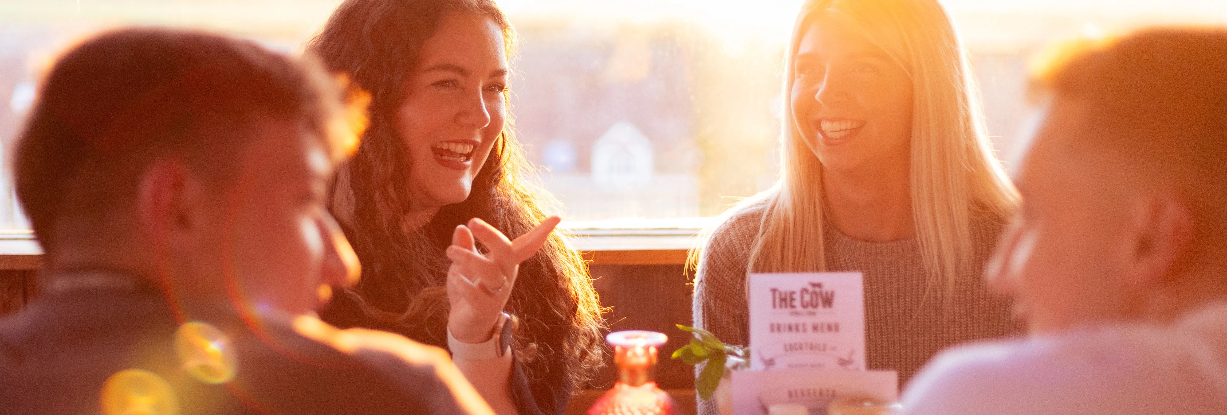 Friends chatting at a table in The Cow restaurant, backlit by warm sunset light