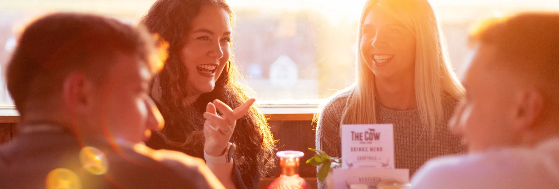 Friends chatting at a table in The Cow restaurant, backlit by warm sunset light