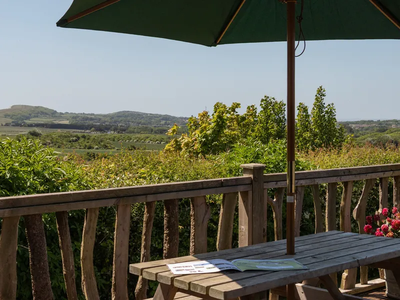 Countryside view from a wooden cabin deck with picnic table and parasol