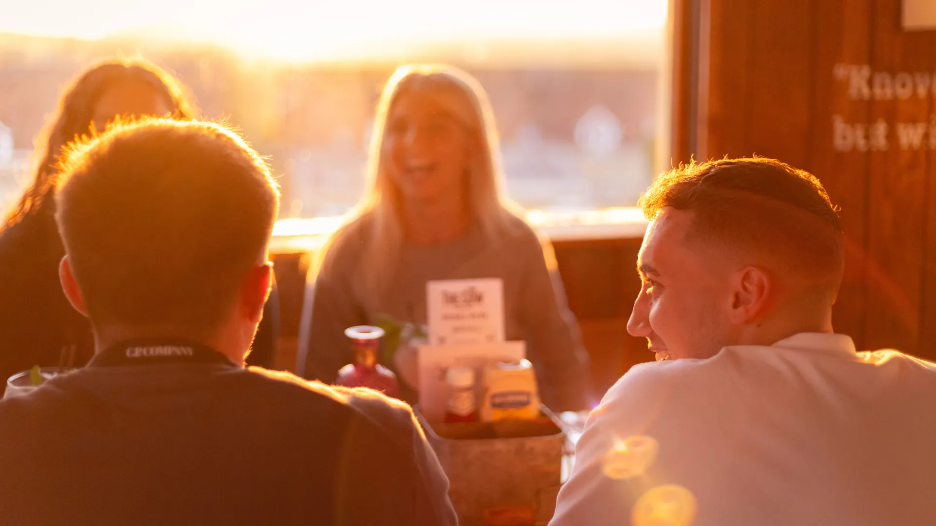 Friends chatting at a table in a cosy restaurant, backlit by warm sunset light