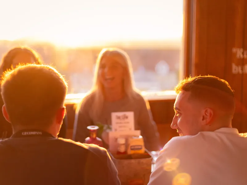 Friends chatting at a table in a cosy restaurant, backlit by warm sunset light