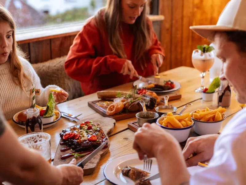 Family enjoying a meal at a rustic wooden table with burgers, chips and sharing platters in a cosy restaurant