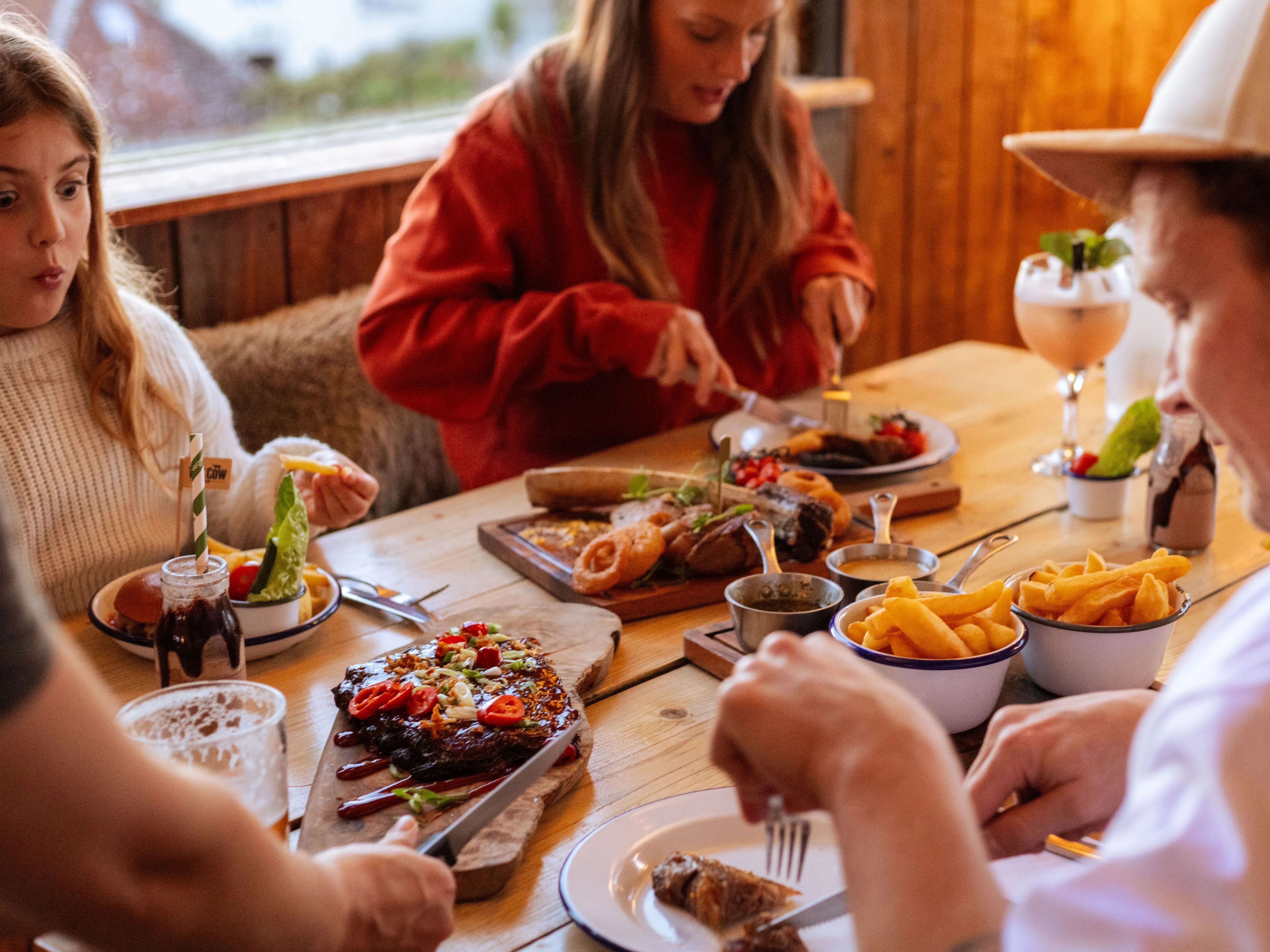 Family enjoying a meal at a rustic wooden table with burgers, chips and sharing platters in a cosy restaurant