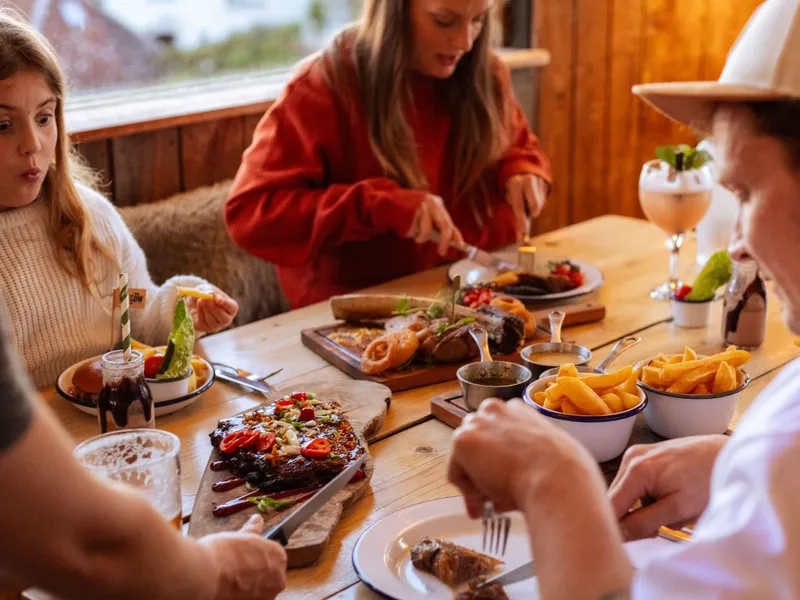 Family enjoying a meal at a rustic wooden table with burgers, chips and sharing platters in a cosy restaurant