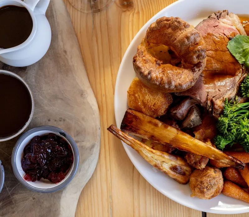 Roast beef Sunday dinner with Yorkshire pudding, roasted parsnips, baby carrots, broccoli and gravy on a white plate