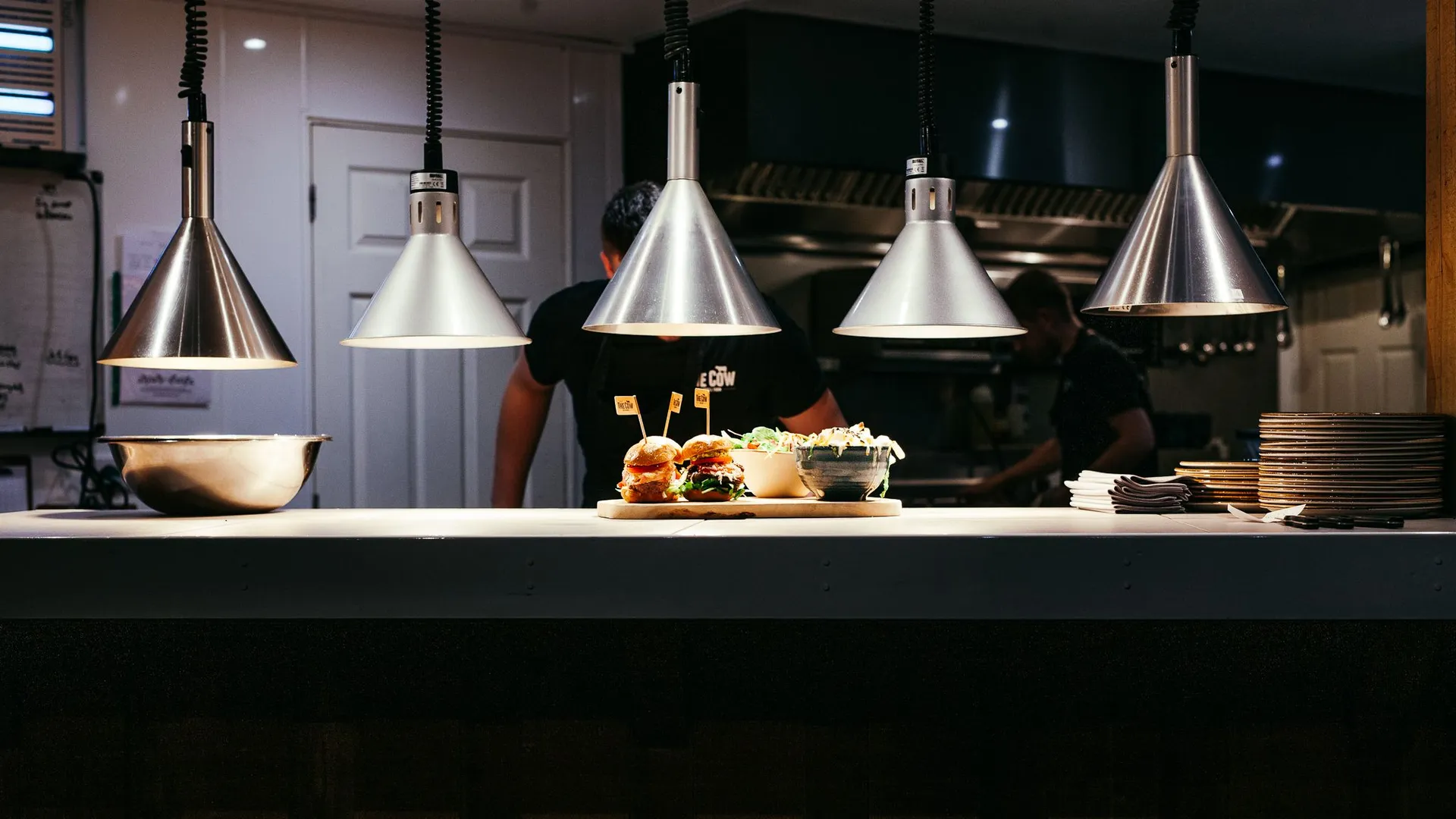 Burgers and sides under silver heat lamps at The Cow kitchen pass, Tapnell Farm