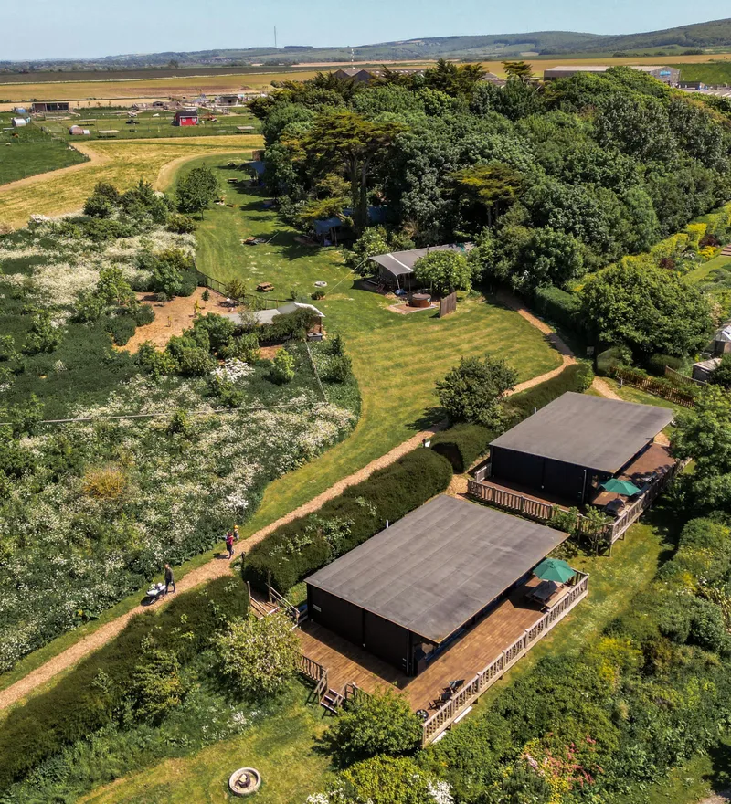 Aerial view of two wooden cabins with decking set among lush gardens and countryside