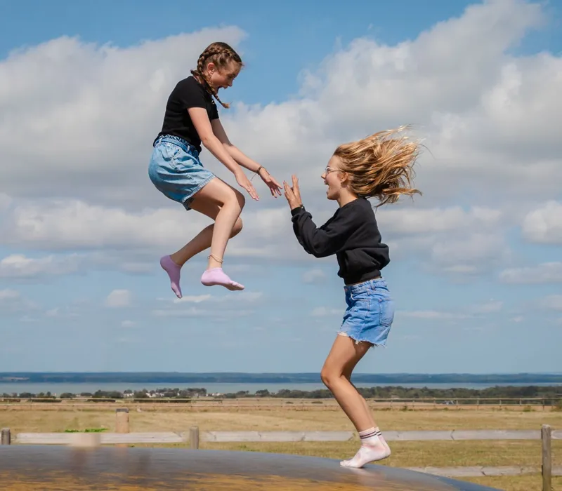 Two girls bouncing on an outdoor inflatable pillow at a farm park on a sunny day