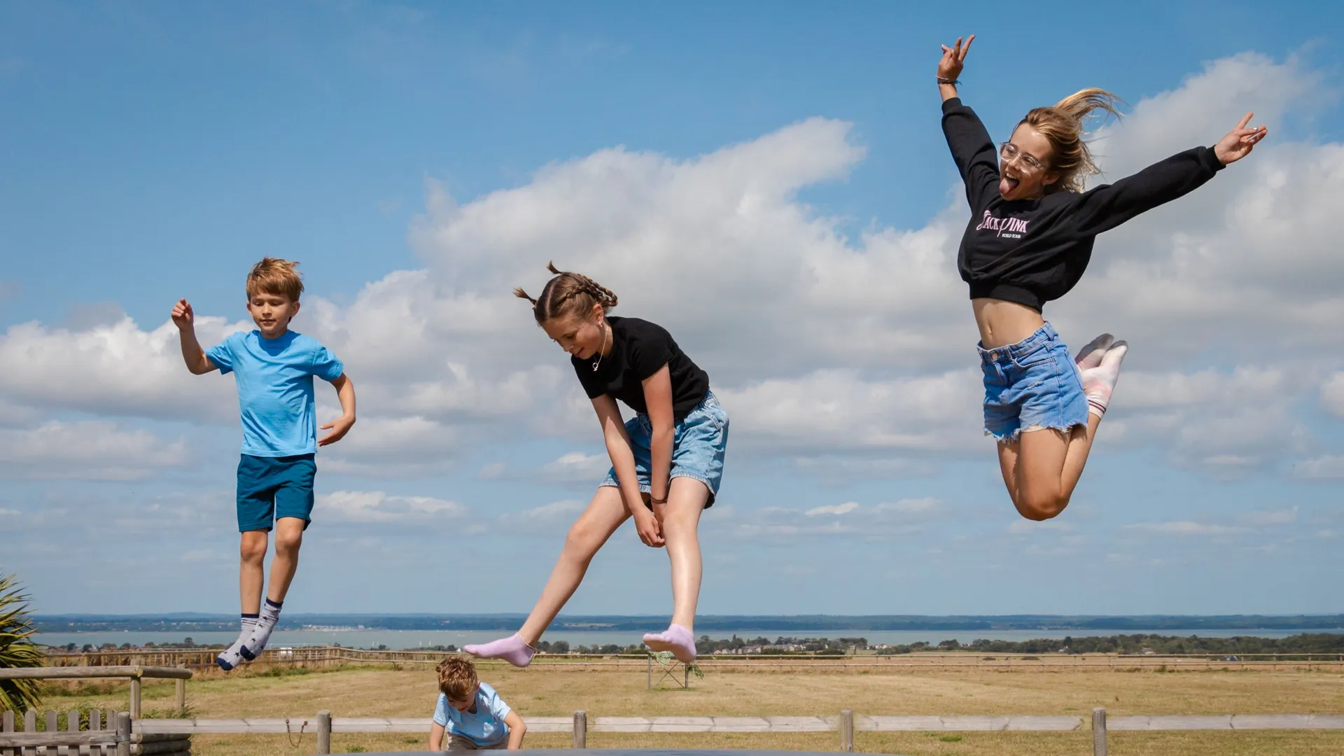 Children and a teenager jumping on an outdoor inflatable pillow at a farm park on a sunny day