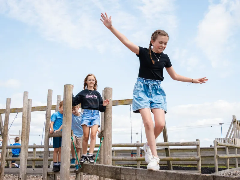 Children balancing on a wooden play structure at a farm park on a sunny day