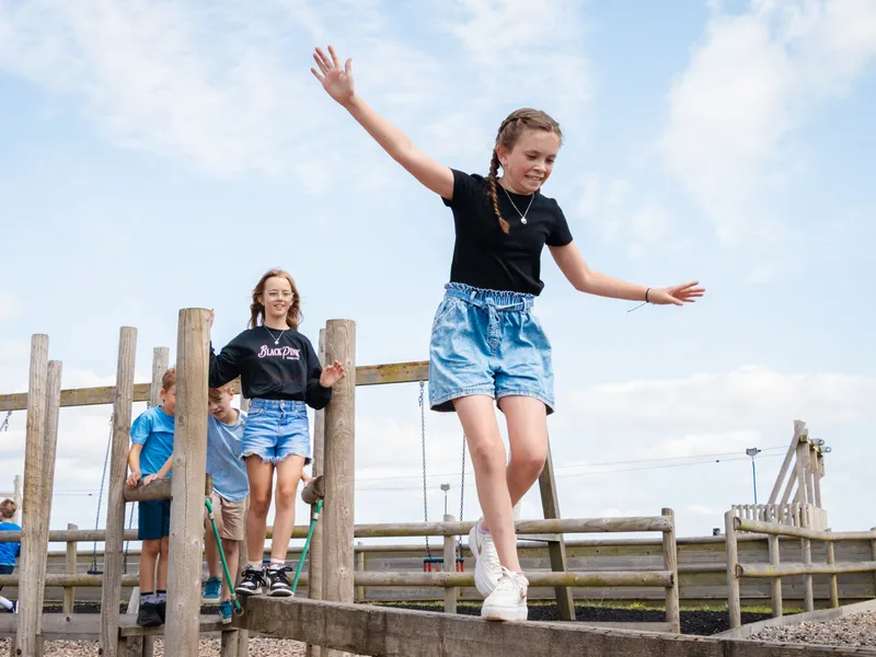Children balancing on a wooden play structure at a farm park on a sunny day