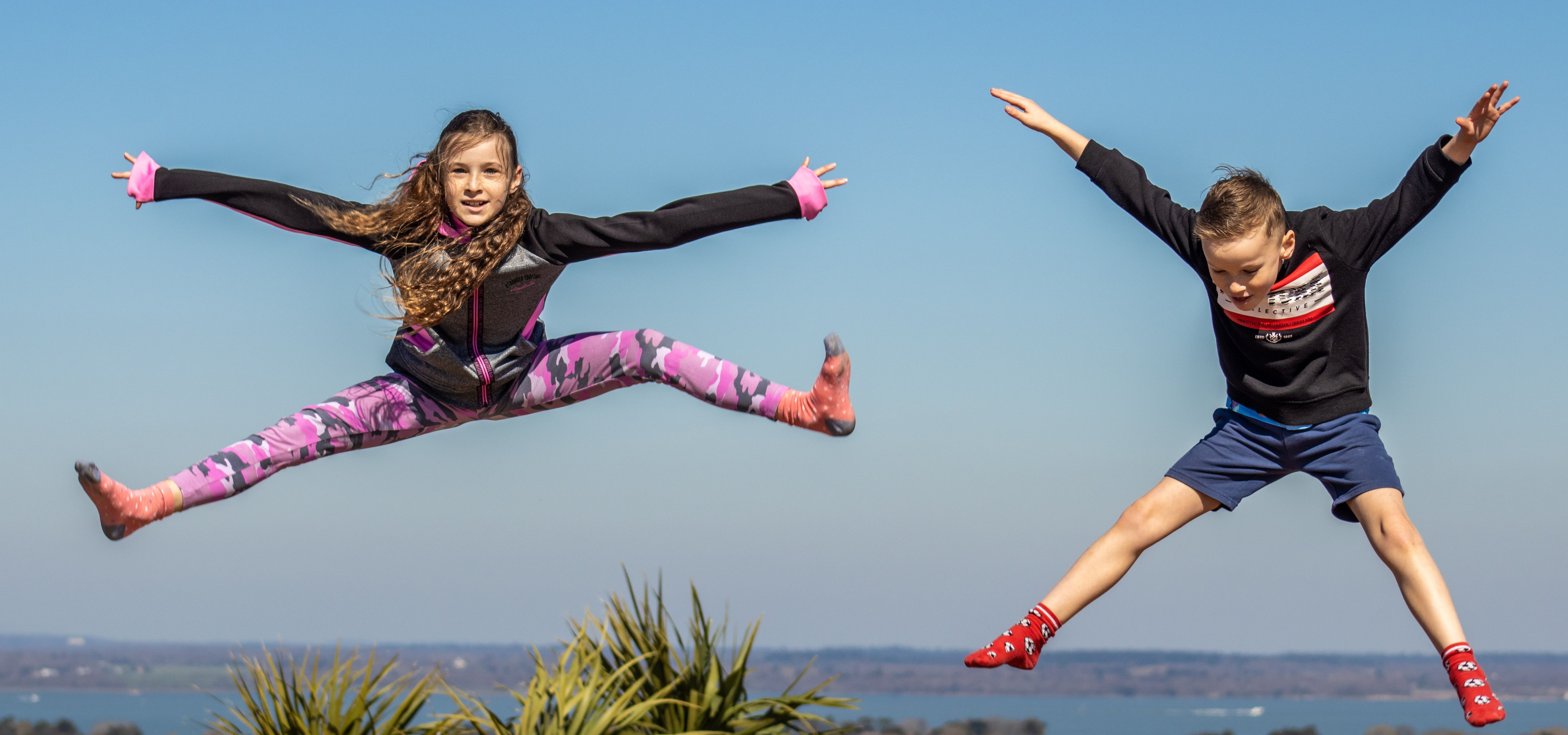 Two children mid-air jumping on a large outdoor bouncy pillow at a farm park on a sunny day