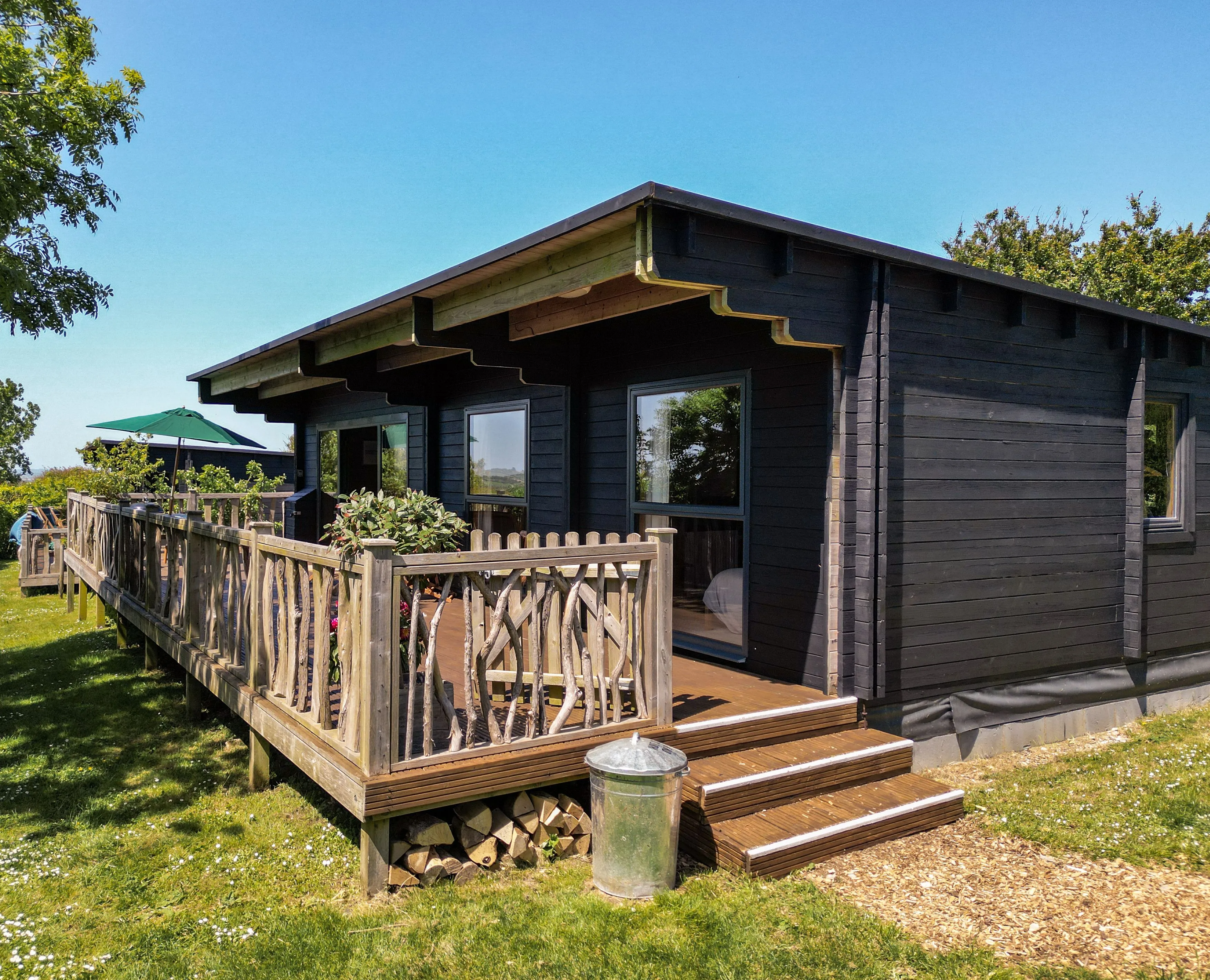 Dark timber cabin with wooden deck and railing on a sunny day