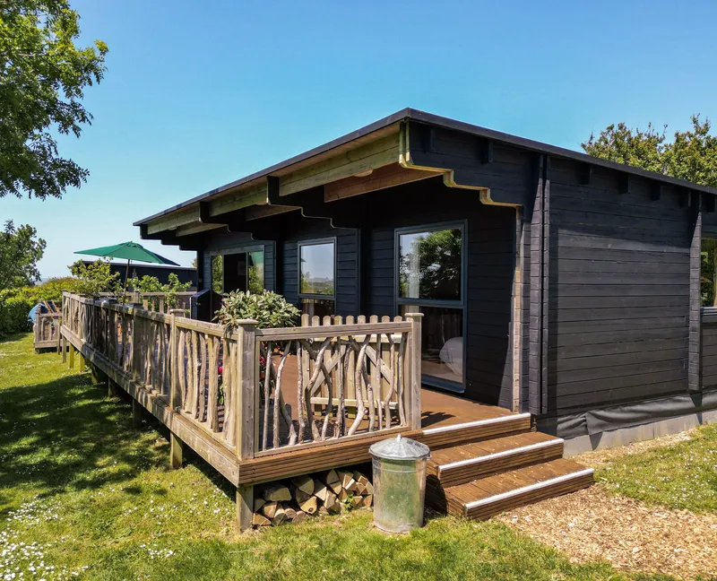 Dark timber cabin with wooden deck and railing on a sunny day