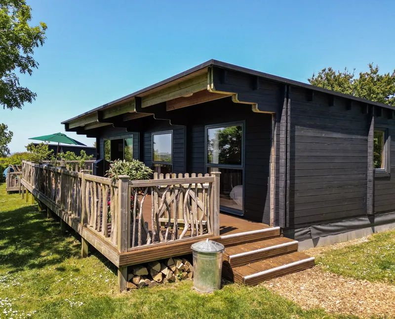 Dark timber cabin with wooden deck and railing on a sunny day