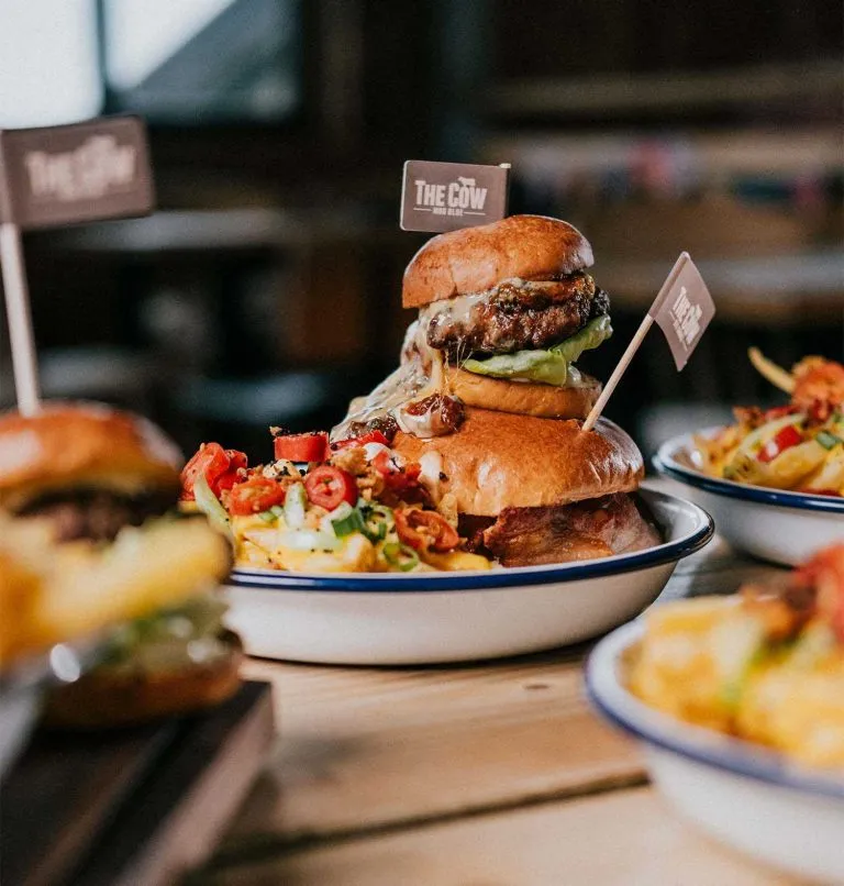 Close-up of a juicy burger with melted cheese, lettuce, and fries served at The Cow Restaurant.