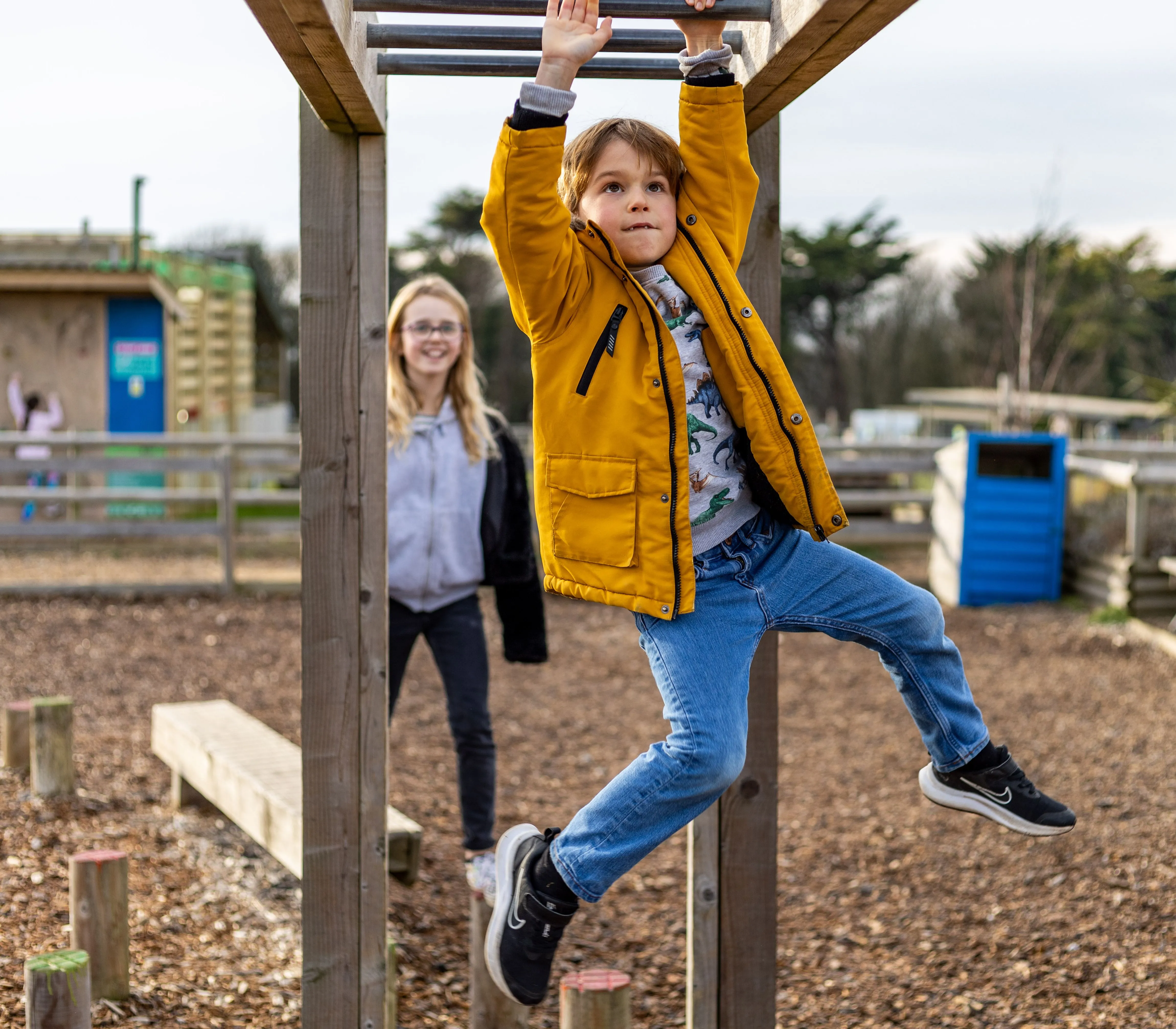 Child in a yellow coat hanging from monkey bars at an outdoor farm park playground