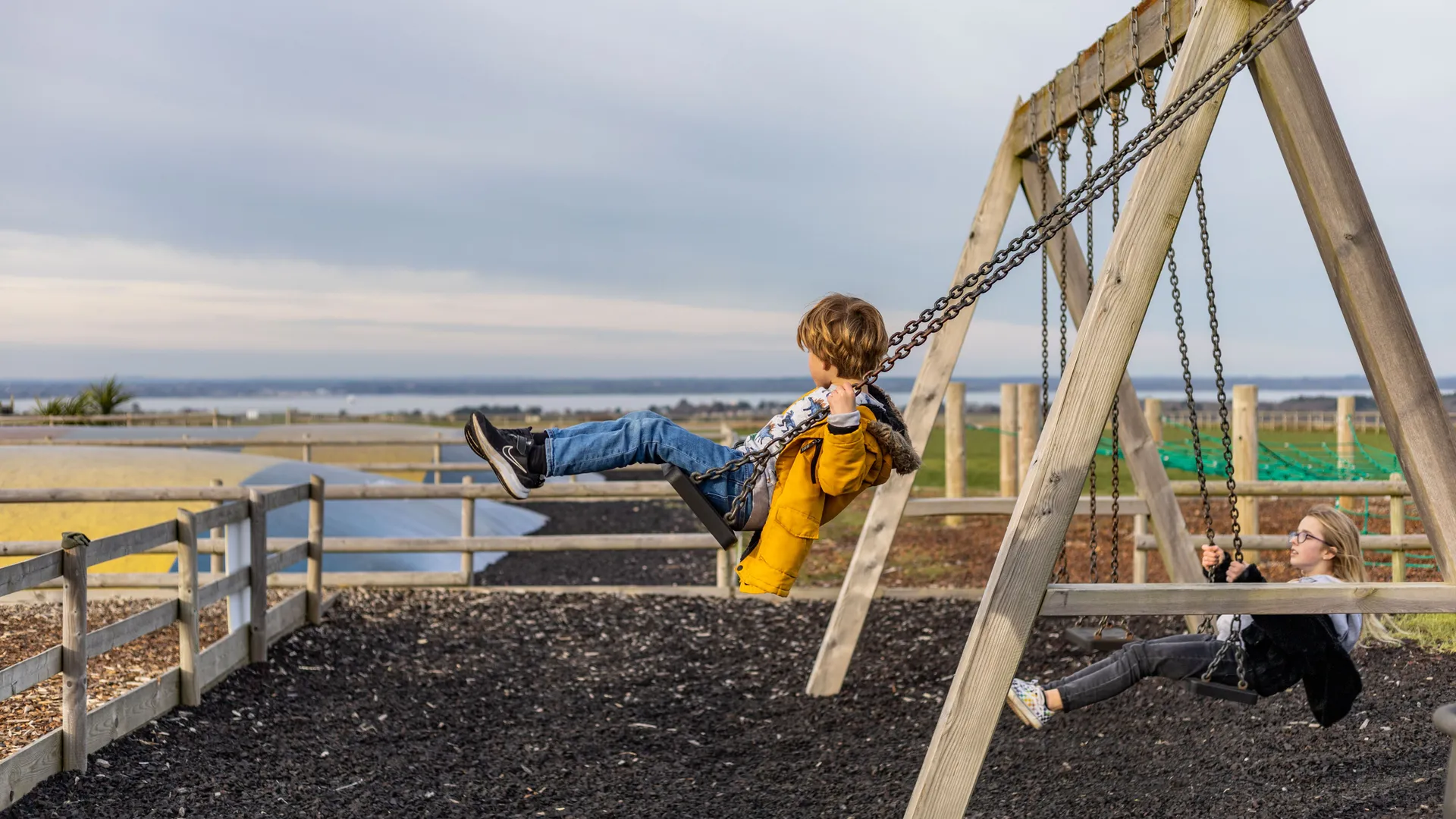 Children swinging on a wooden swing set at a farm park in winter