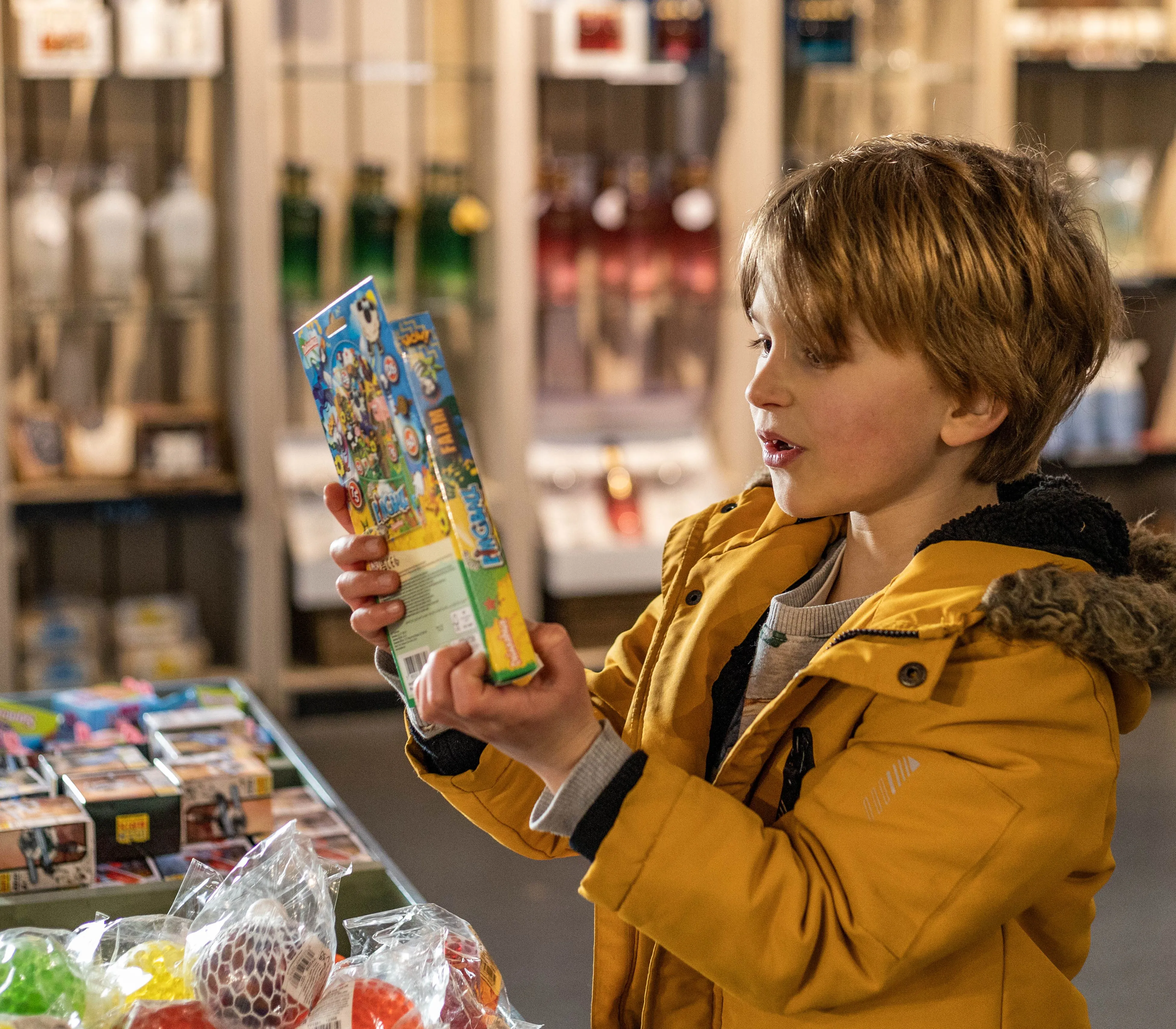Child in a yellow coat examining a colourful toy box in a farm park gift shop
