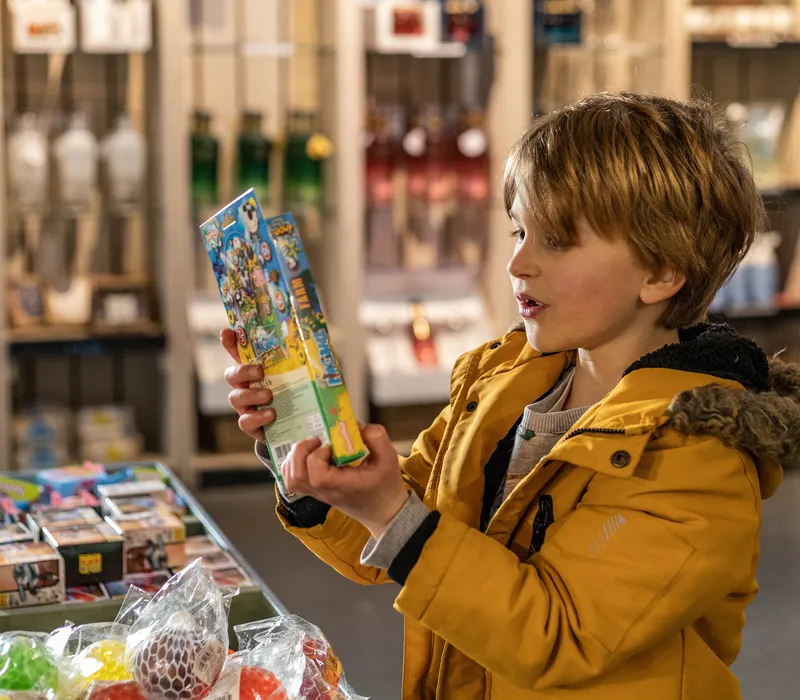 Child in a yellow coat examining a colourful toy box in a farm park gift shop