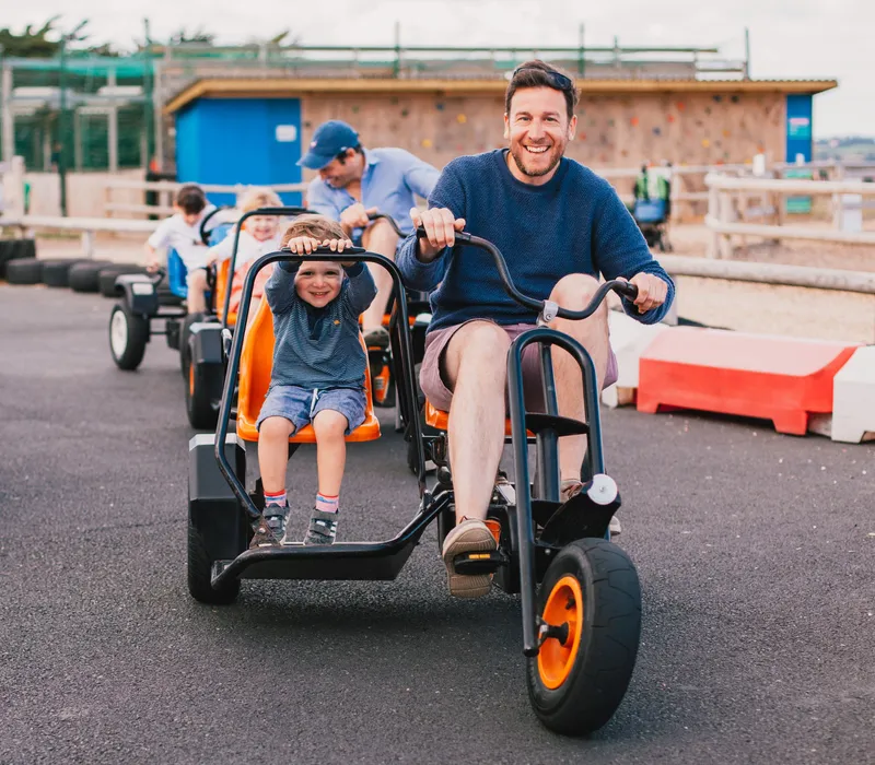 Father and child riding a pedal go-kart on an outdoor track