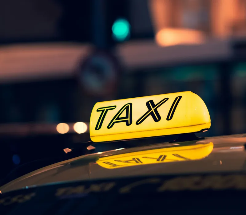 Illuminated yellow taxi sign on a car roof at night