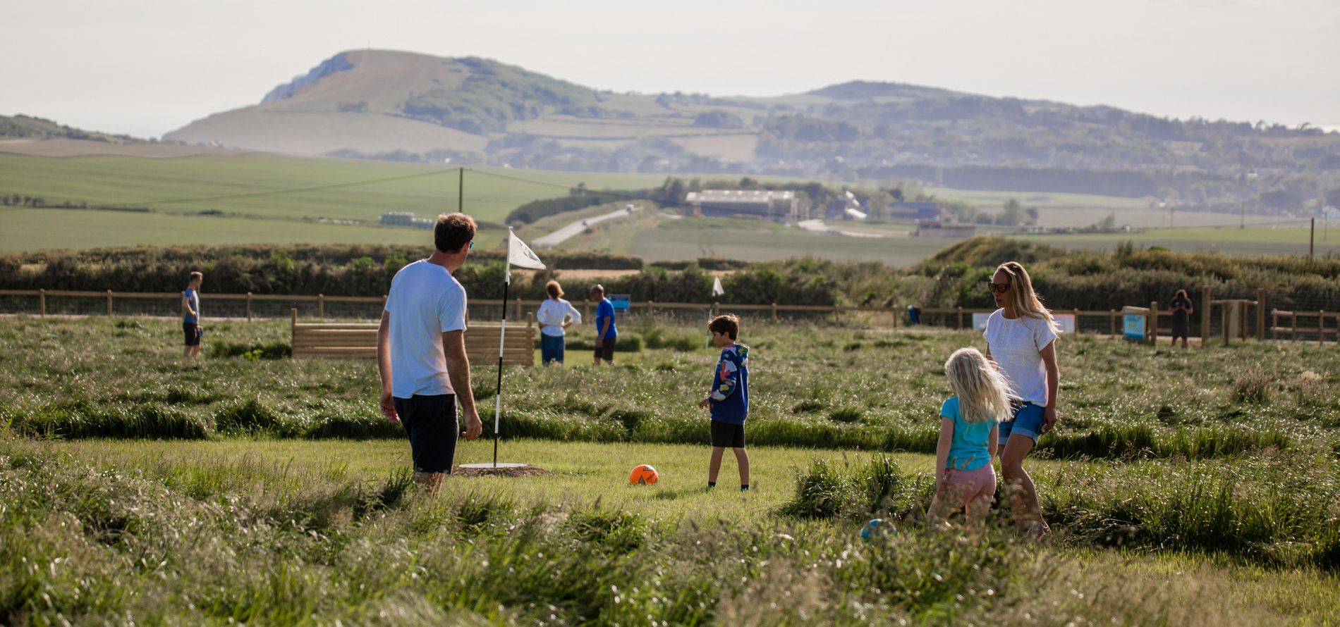 Family playing football on a grassy field with hills in the distance