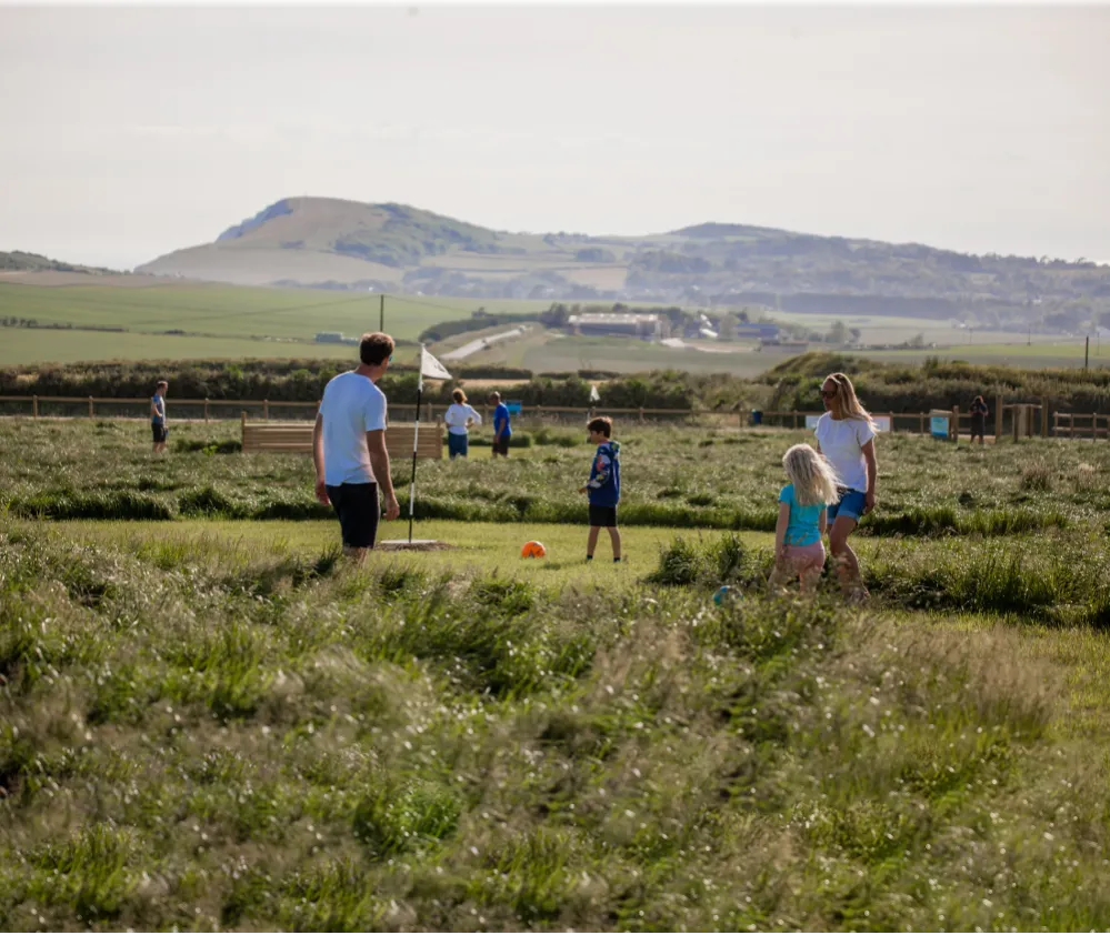 Family playing football on a grassy field with hills in the distance