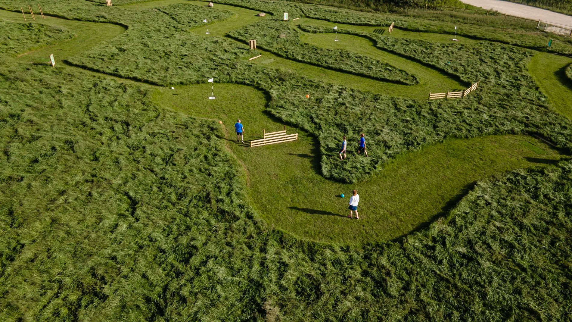 Aerial view of people playing footgolf on a grassy course with winding fairways and small flags.