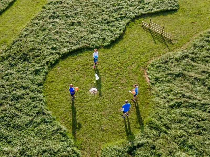 Aerial view of four people playing a lawn game around a flag on a grassy field.