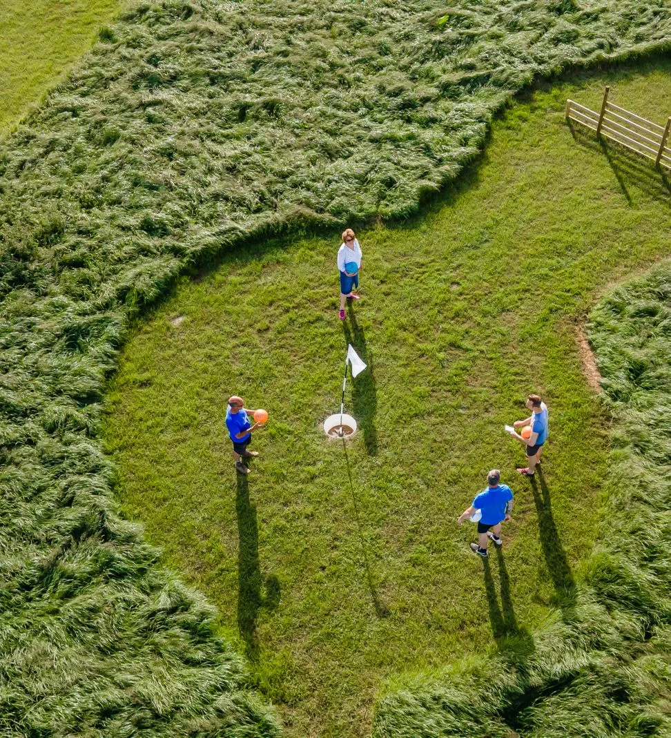 Aerial view of four people playing a lawn game around a flag on a grassy field.