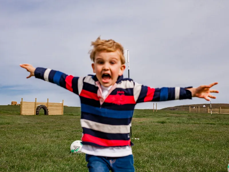 Excited young boy running with arms outstretched on a grassy field