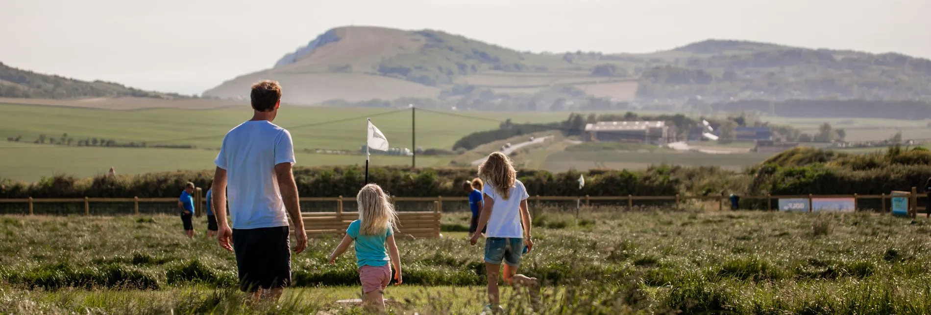 A man and two children walking through a grassy field with hills in the background