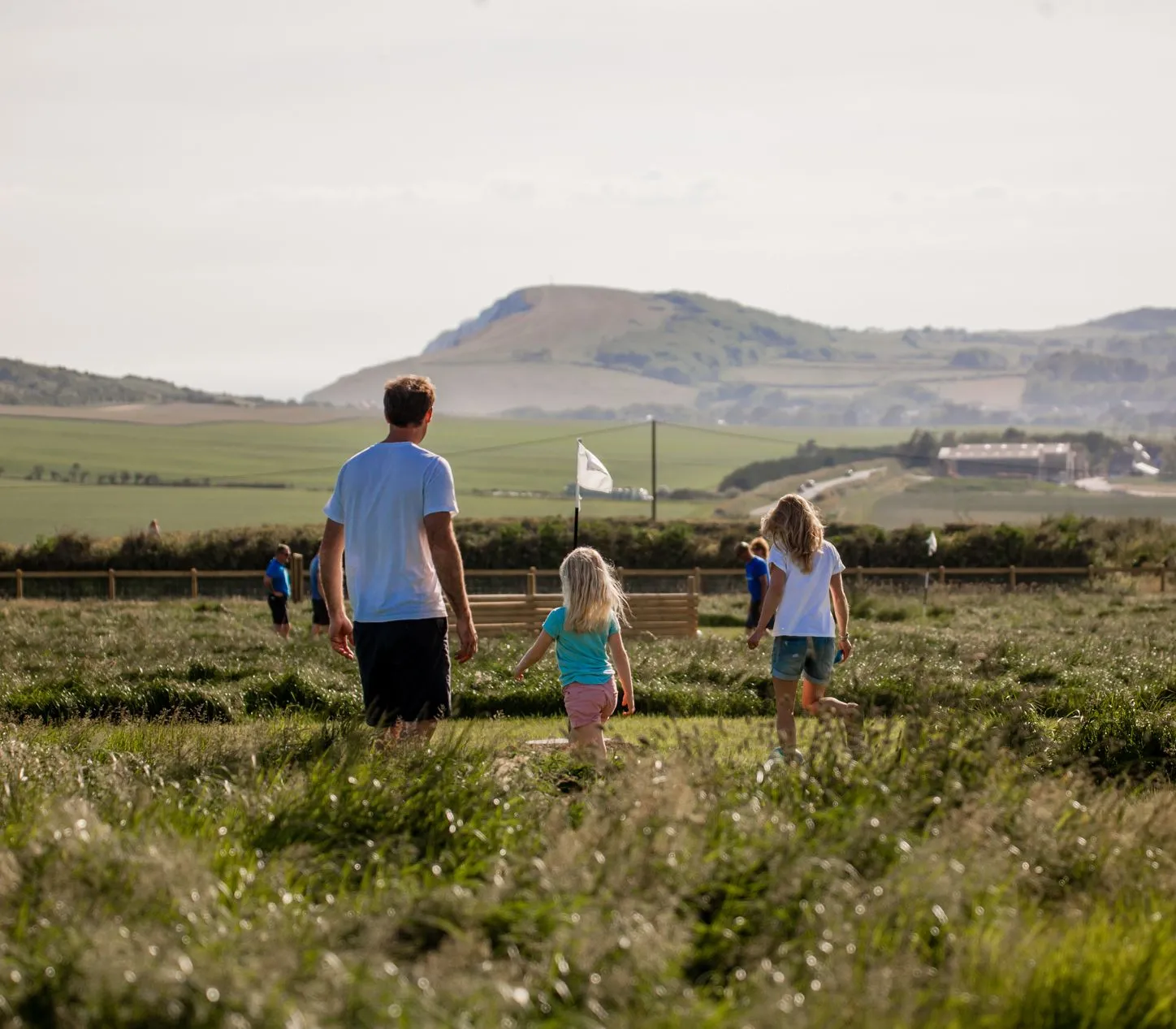 A man and two children walking through a grassy field with hills in the background
