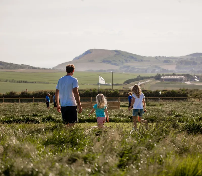 A man and two children walking through a grassy field with hills in the background