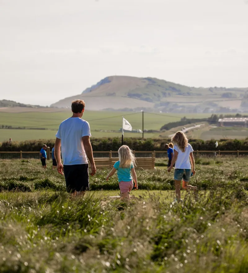 A man and two children walking through a grassy field with hills in the background