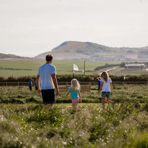 A man and two children walking through a grassy field with hills in the background
