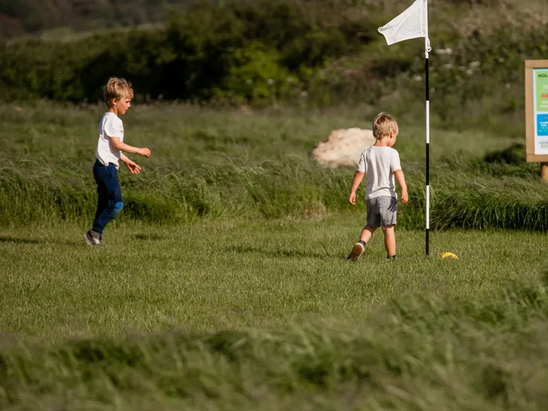 Two children walking on a grassy golf course near a white flag and a hole sign
