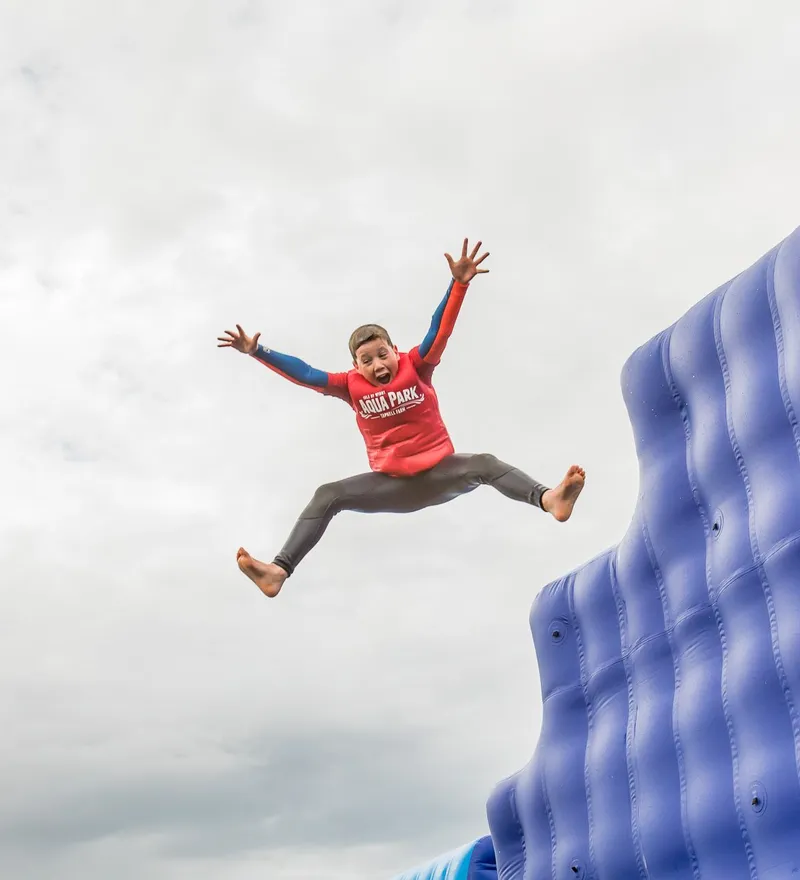 Child leaping off a large blue inflatable water slide with arms outstretched
