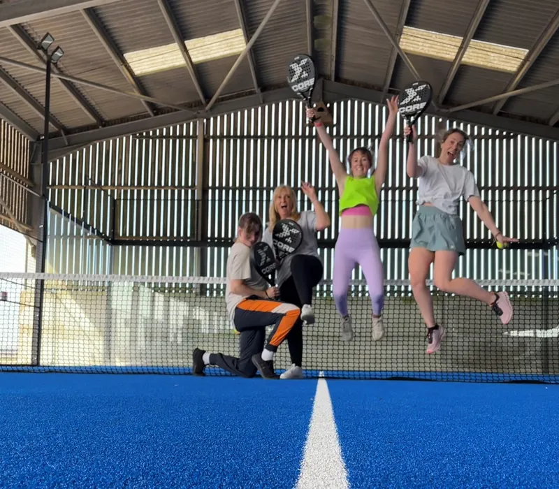 Group of friends jumping and celebrating on an indoor padel court holding rackets