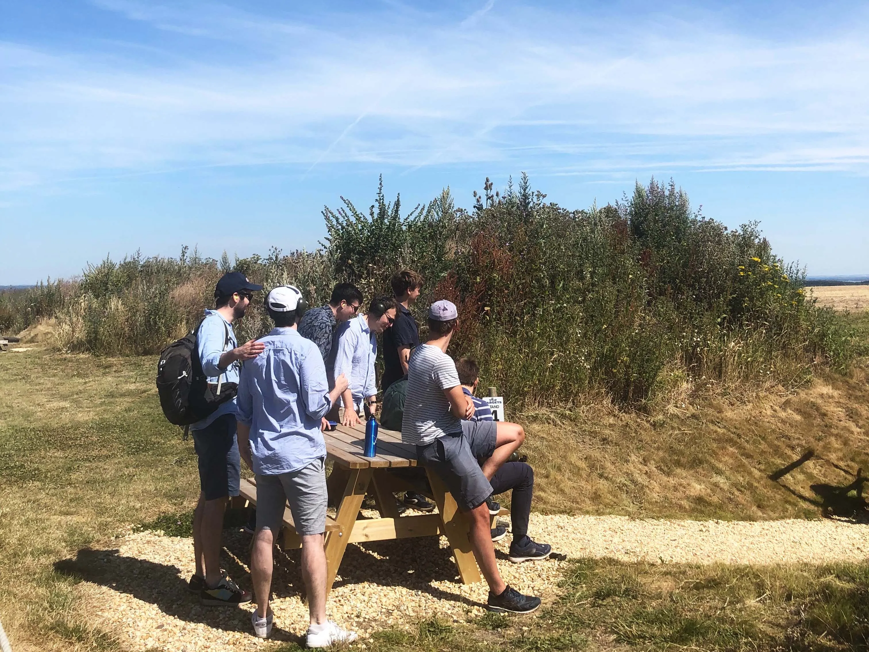 Group of friends gathered around a picnic table in a grassy field under a clear blue sky