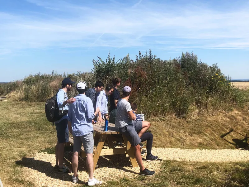Group of friends gathered around a picnic table in a grassy field under a clear blue sky