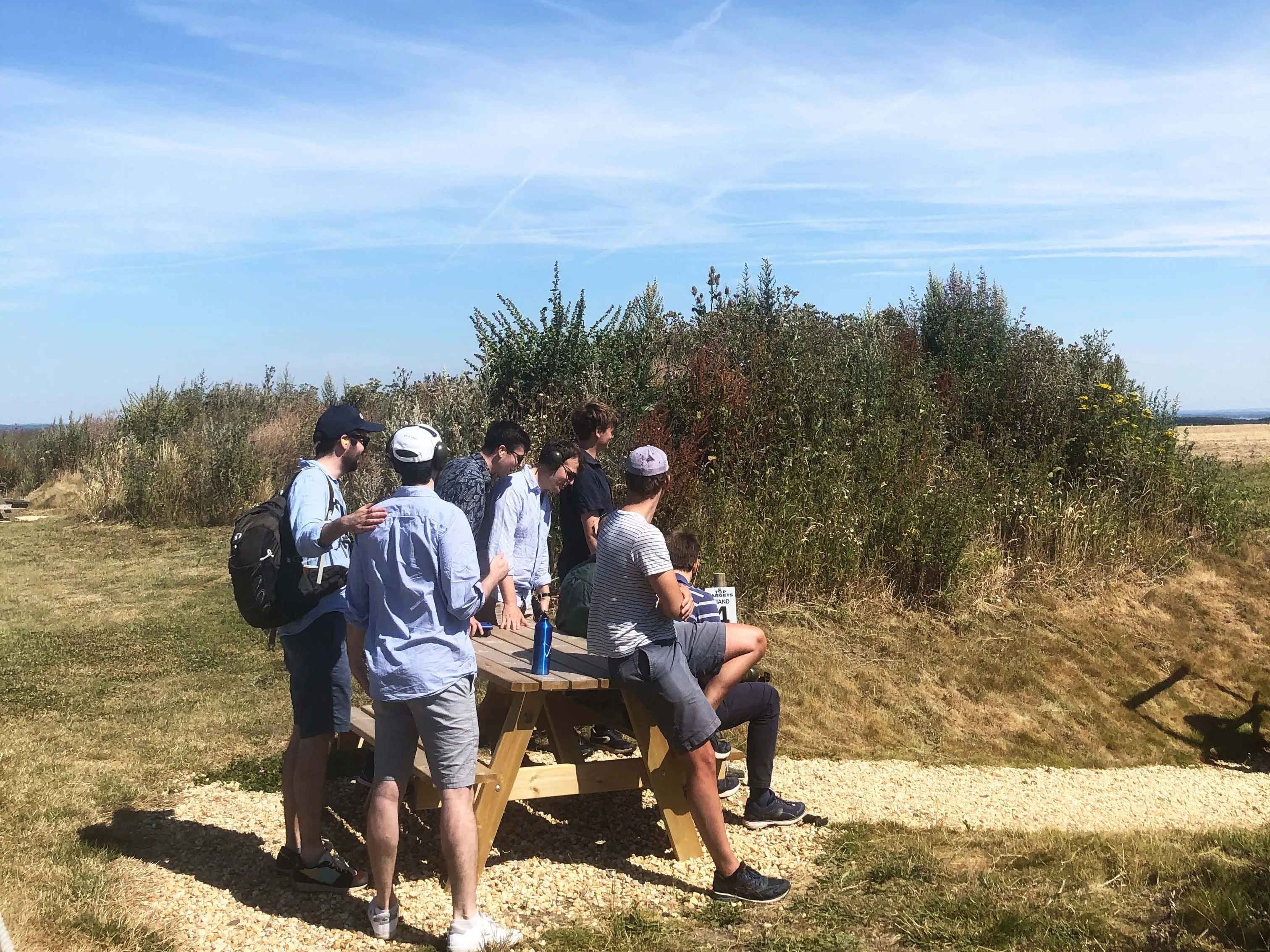 Group of friends gathered around a picnic table in a grassy field under a clear blue sky