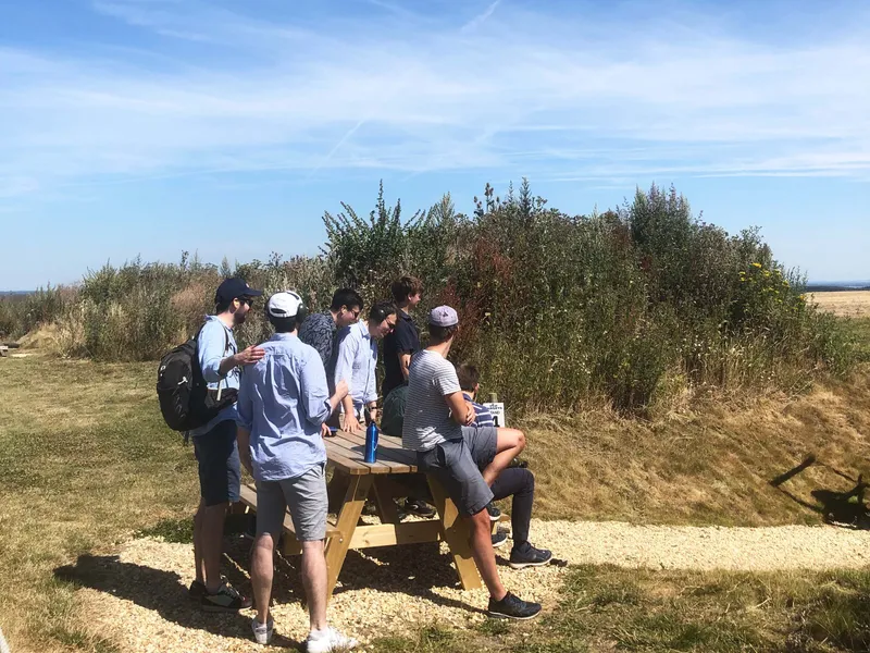 Group of friends gathered around a picnic table in a grassy field under a clear blue sky