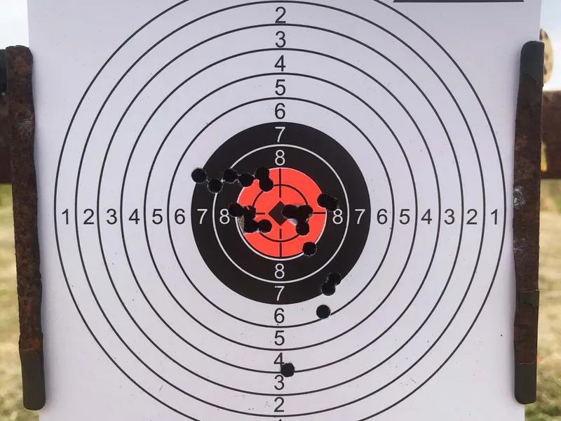 Paper shooting target with concentric scoring rings and clustered bullet holes near the centre