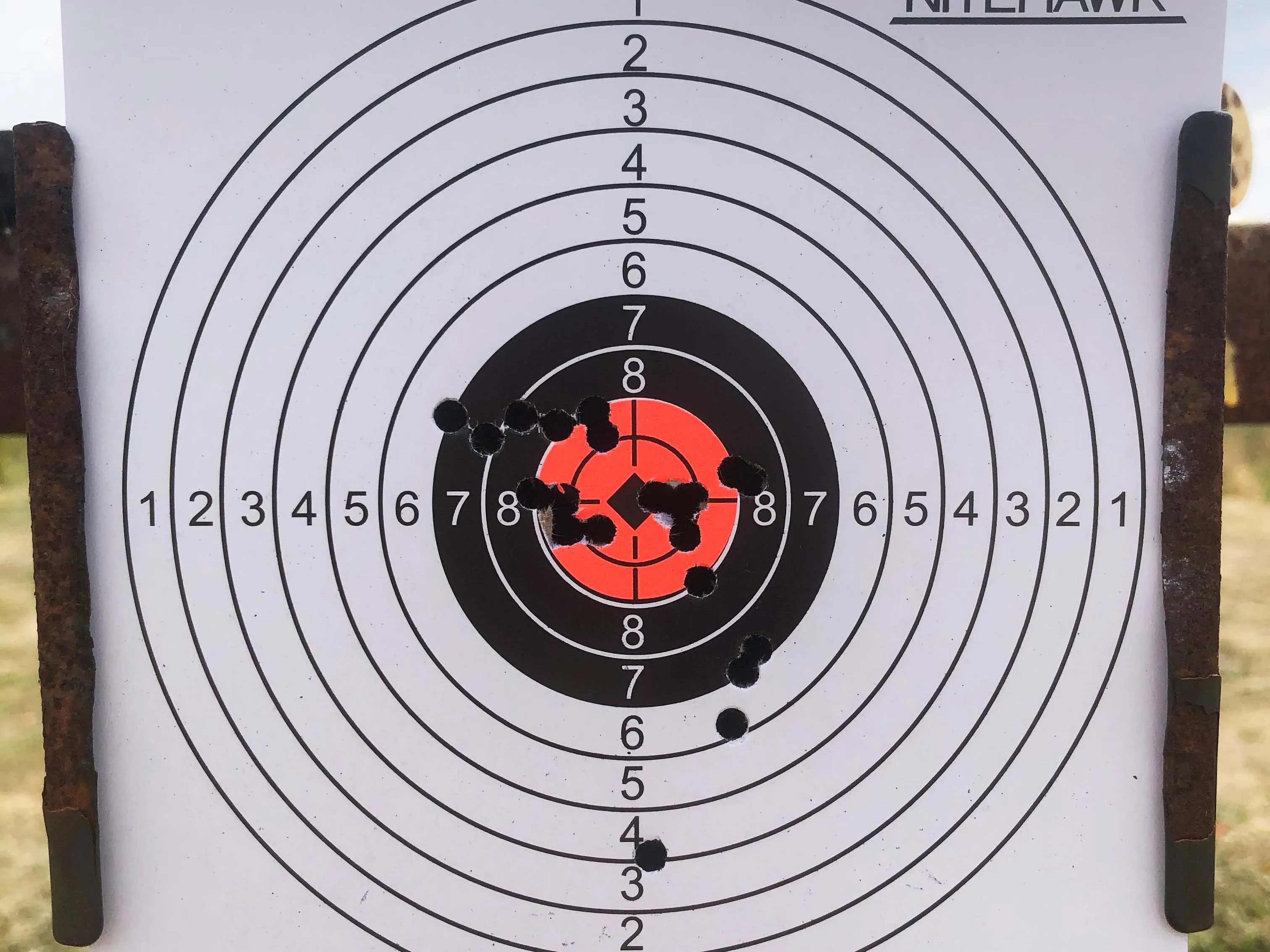 Paper shooting target with concentric scoring rings and clustered bullet holes near the centre