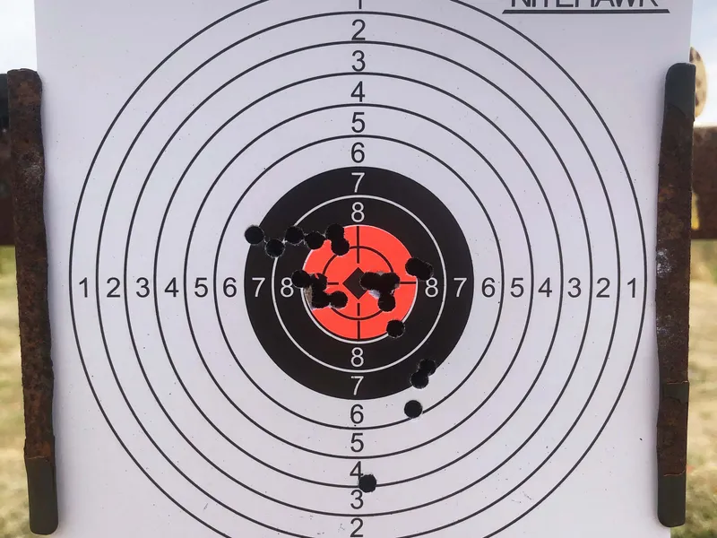 Paper shooting target with concentric scoring rings and clustered bullet holes near the centre