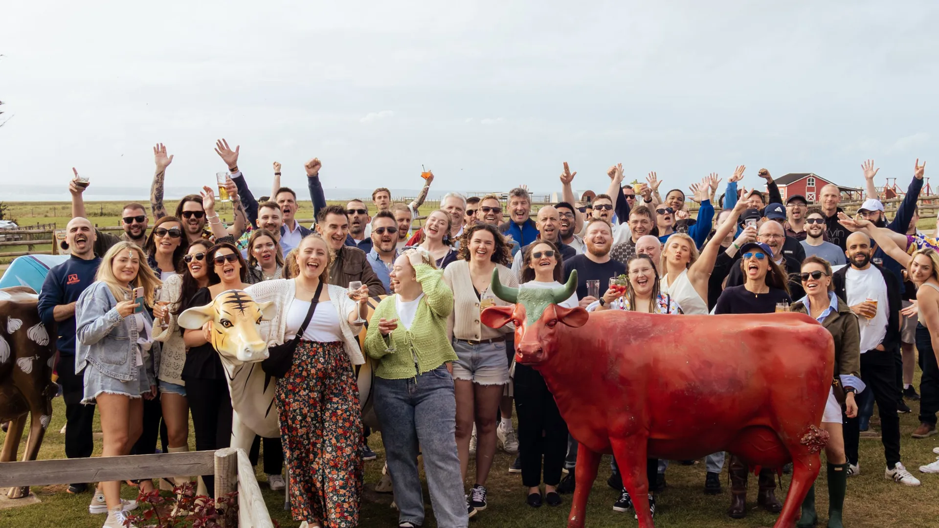 Large group of people cheering outdoors beside painted cow statues on a grassy field