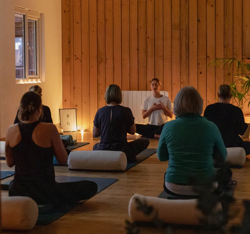 Group meditation class in a warm, candle-lit studio with wooden walls