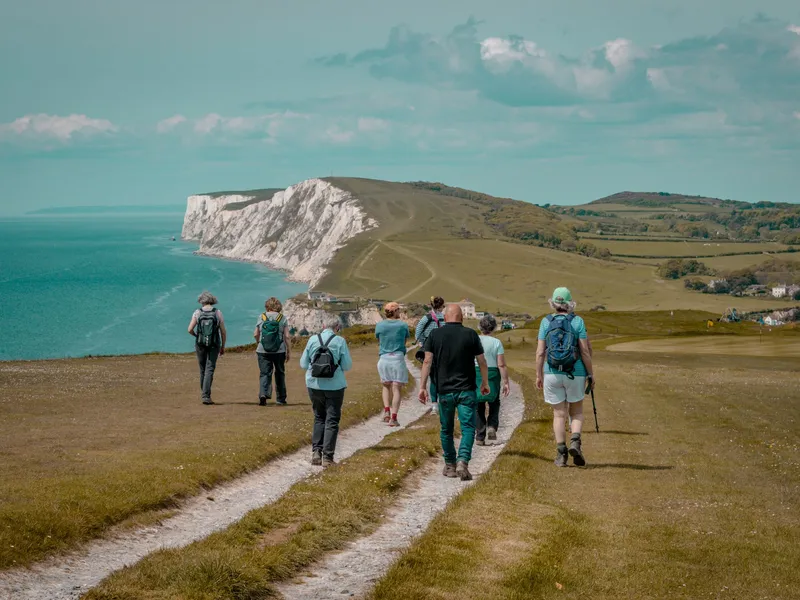 Group of hikers walking along a coastal path towards white chalk cliffs above a turquoise sea